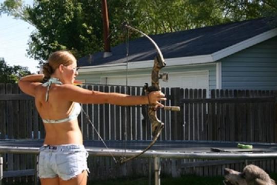 Woman aiming a compound bow outdoors