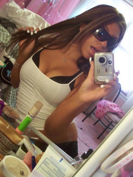 Woman in white tank top takes a mirror selfie with a digital camera