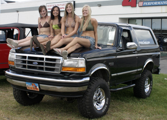 Black Ford Bronco, 3q-front view, with four women on hood. "STATE COUNTRY" sticker on rear window