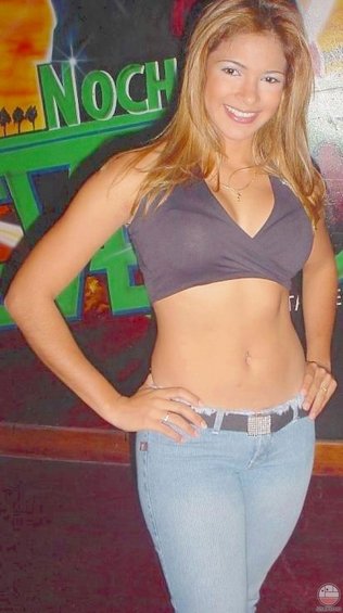 Woman in a grey crop top and light blue jeans with a jeweled belt, standing in front of a mural