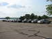 2003 Ford Crown Victoria - A row of sedans, including a 2003 Ford Crown Victoria, are parked in a lot near a body of water.