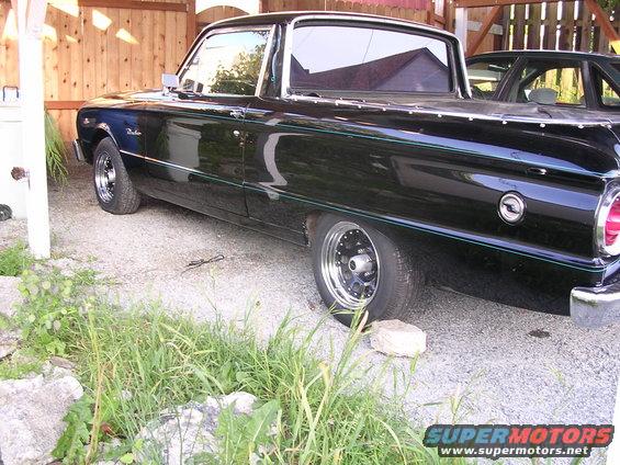 Black 1963 Ford Ranchero, side view, with chrome trim and aftermarket wheels, parked on gravel