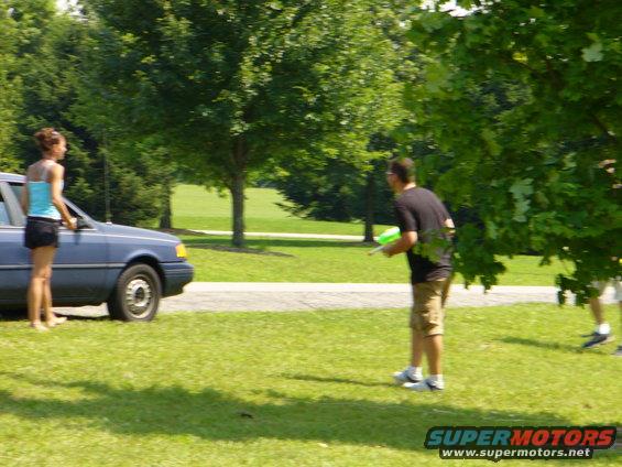 Blue sedan parked on grass, woman standing by driver's door