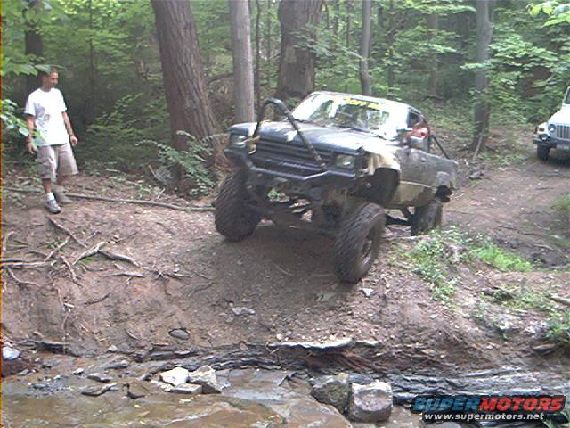 Modified off-road truck climbing a dirt incline, another Jeep visible in background