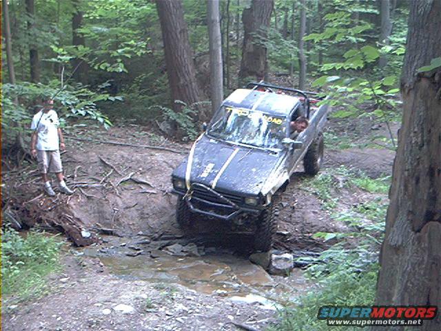 1986 Toyota pickup truck off-roading, driver visible, person standing nearby