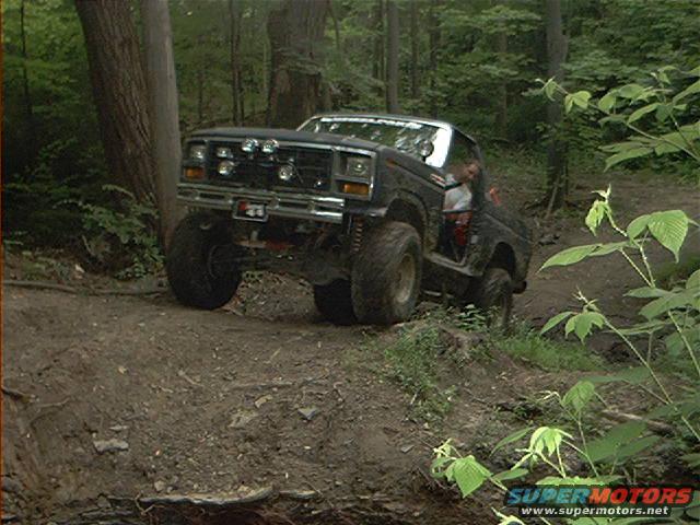 Black off-road SUV with large tires on a dirt trail, driver visible
