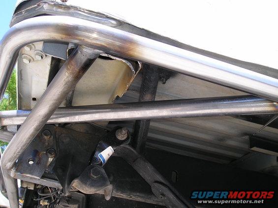Close-up of custom metal tubing welded to a vehicle's frame, showing suspension parts and a blue and white label