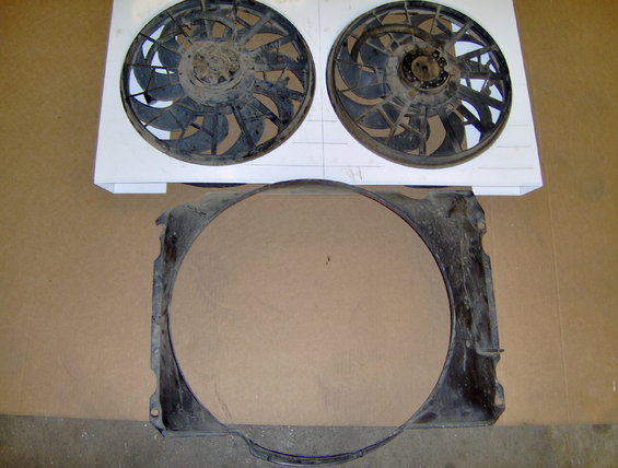 Radiator fan shroud and two electric fans laid out on a cardboard surface