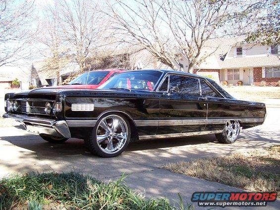 1966 Mercury Monterey coupe, black paint, chrome wheels, parked in driveway. Red vehicle behind it