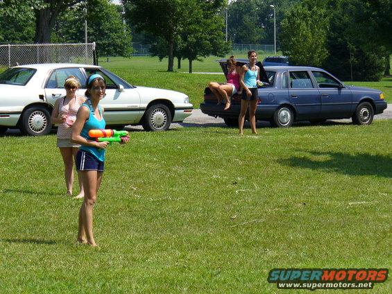 Two sedans parked on a lawn with three women standing around one of them