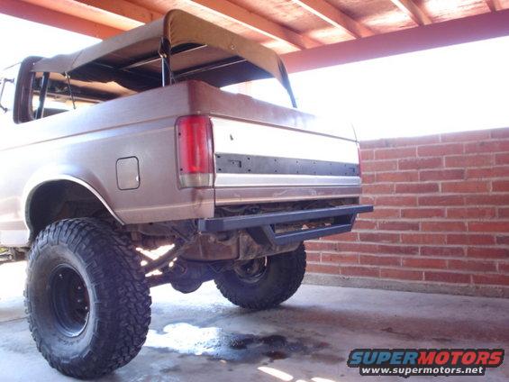 Rear view of a lifted, brown Ford Bronco with a soft top removed, parked under a cover