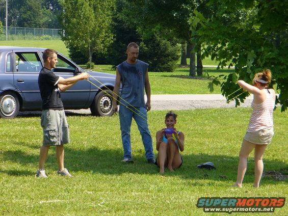 Blue sedan parked on grass, people holding slingshots