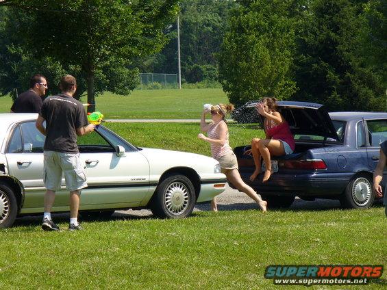 Two cars parked on grass, people with water guns