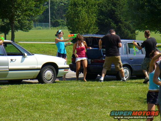 People with water guns by cars on a sunny day