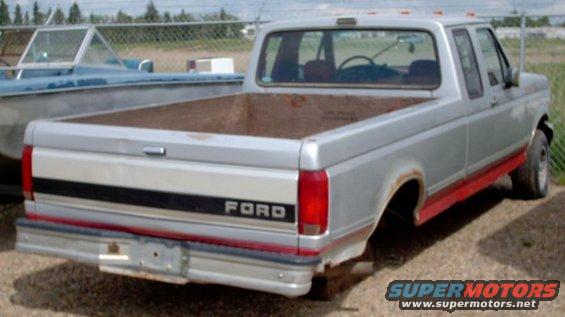 Rear view of a silver Ford pickup truck with red trim, missing rear wheels