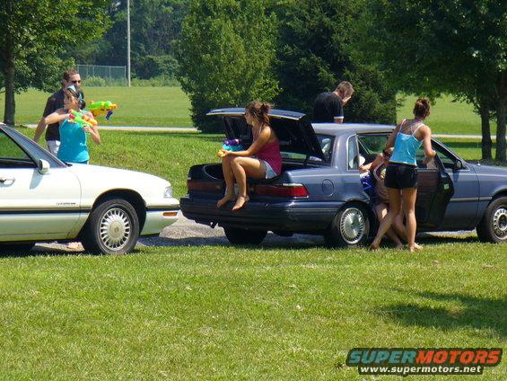 Two cars parked on grass, people with water guns around them