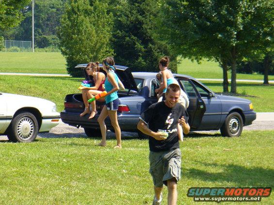 Blue sedan with open trunk and doors, people holding water guns