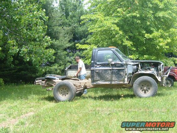 Black pickup truck chassis with cab, missing front clip and bed, parked on grass