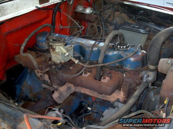 Engine bay with blue valve covers, carburetor, and rusty exhaust manifolds
