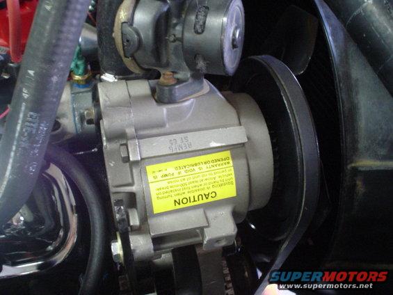 Close-up of a power steering pump with a yellow caution sticker and a belt