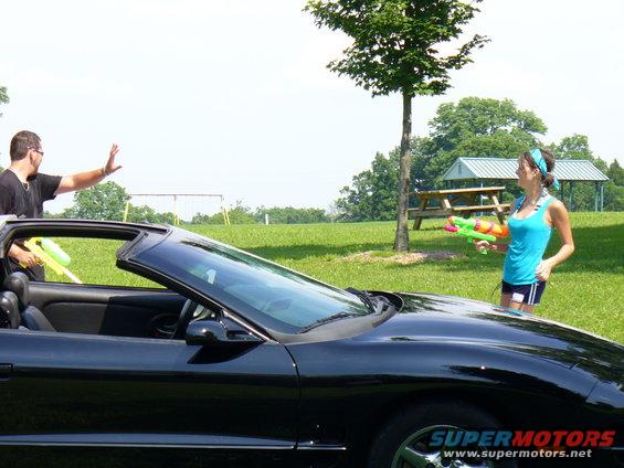 Black convertible sports car with a man and woman holding water guns