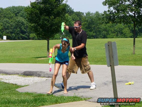 Two people are having a water gun fight in a park, one person is spraying the other