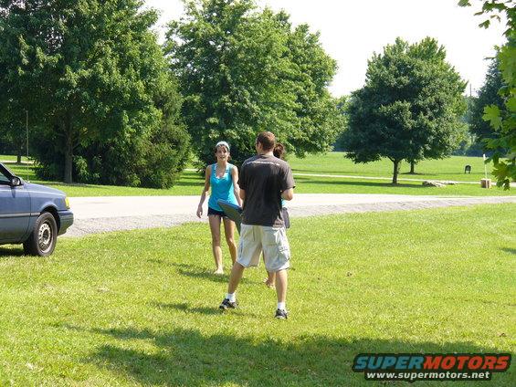 Blue sedan parked on grass with two people standing nearby