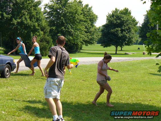 People with water guns in a park, one person carrying a blue object
