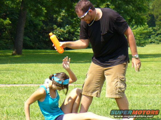 Man holding orange bottle over woman sitting on grass