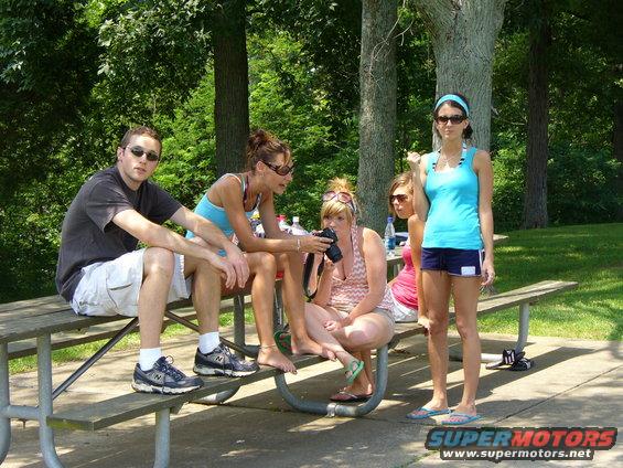 Group of young adults sitting and standing around a picnic table in a park