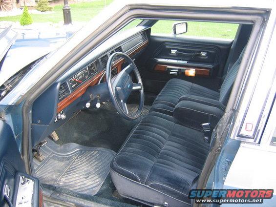 Blue velour interior of a 1980s sedan, showing dashboard, steering wheel, and front seats