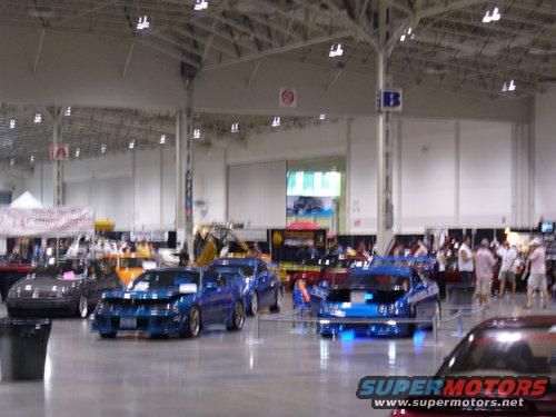 Indoor car show with several modified cars on display, including blue and gray sedans