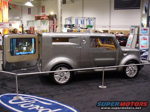 Gray concept van with rear door open displaying a city skyline on a screen, silver wheels, yellow interior visible