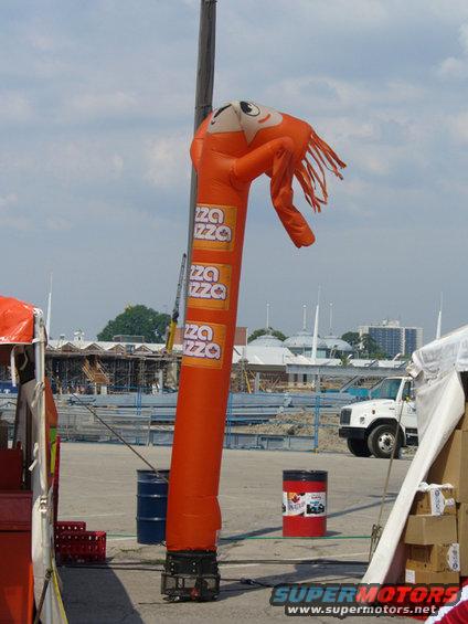 Orange inflatable tube man with pizza logos stands next to a white truck at a construction site