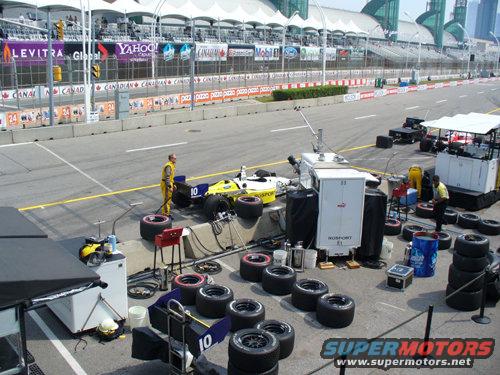 Race car with crew and tires on pit lane, grandstands in background