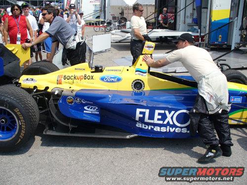 Race car with yellow and blue livery, "FLEXO abrasives" text visible on side. People in racing suits are near it