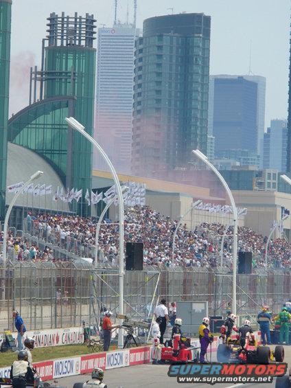 Race cars on track with crowd in stands and city skyline