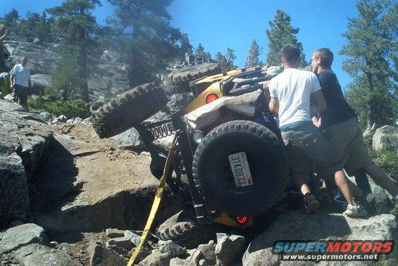 Yellow 1966 Jeep CJ5 tilted on its side on a rocky trail with two people pushing it