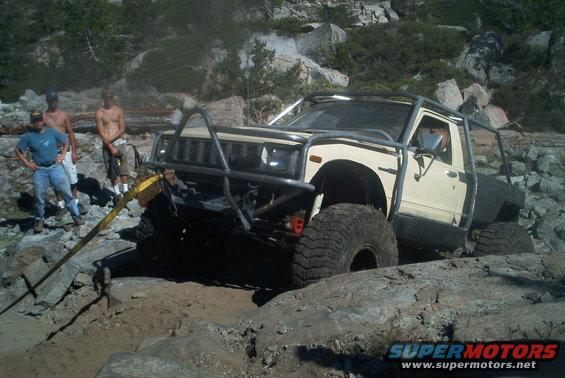 Cream-colored pickup truck with a roll cage navigating rocky terrain