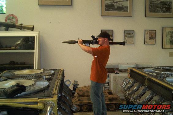Man with rocket launcher in museum with tank models and engine parts