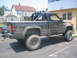 1990 Ford Bronco - A muddy black pickup truck with a roll bar is parked outside a building.