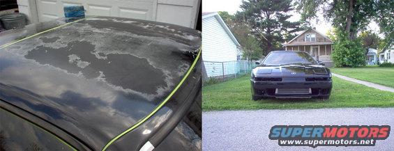 Front view of a black sports car parked on grass in front of a house. The car has a custom front bumper and a large intercooler. The paint on the roof of another car is peeling