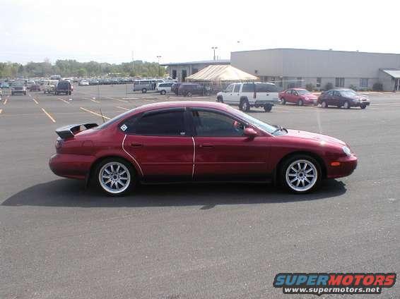 Red 1998 Ford Taurus sedan with a rear spoiler and aftermarket wheels, viewed from the side