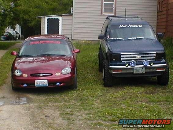 Red 1998 Ford Taurus parked next to a lifted blue Chevrolet S-10 Blazer
