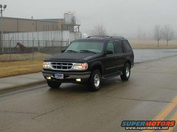 Black Ford Explorer SUV parked on wet asphalt, front 3/4 view