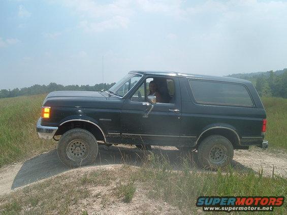 1988 Ford Bronco side view, driving on a dirt path with grassy hills in background