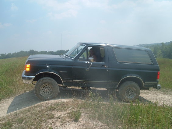Dark blue Ford Bronco driving on a dirt path in a grassy field