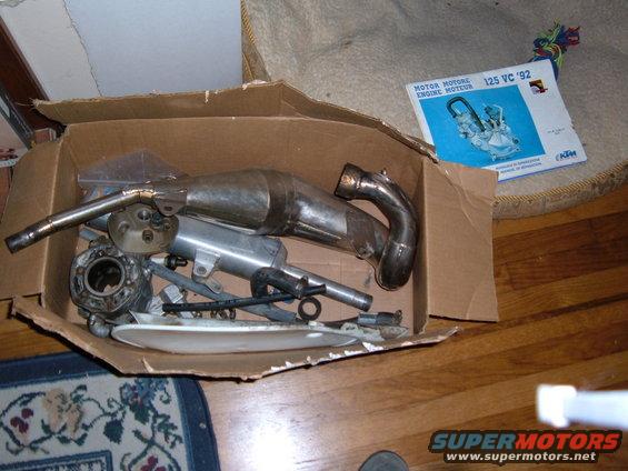 Motorcycle exhaust pipe and engine parts in a box with a 1992 KTM manual