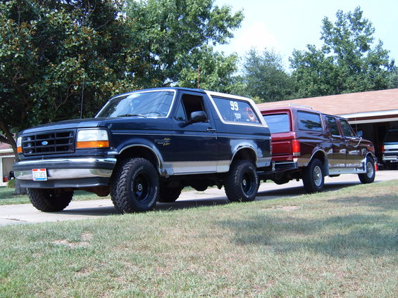 Dark blue Ford Bronco with silver trim, towing a red Ford Econoline van