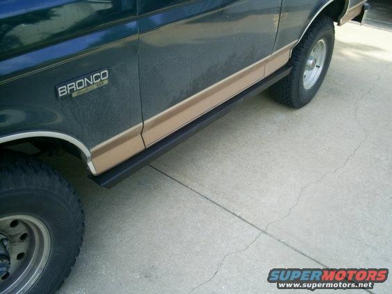 Dark green and tan Ford Bronco side with black step bars and chrome trim